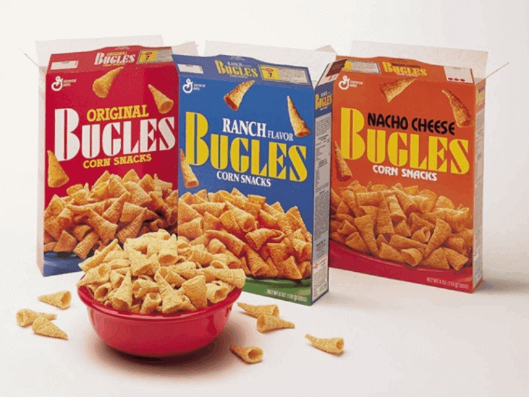 A red bowl of Bugles with three vintage front facing boxes of Bugles behind it. Original Bugles Corn Snacks, Ranch Bugles Corn Snacks and Nacho Cheese Bugles Corn Snacks